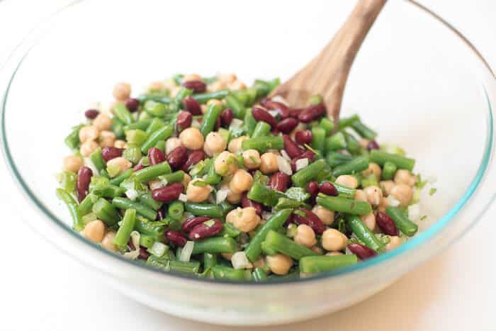 The salad is mixed together with a wooden spoon in a glass mixing bowl.