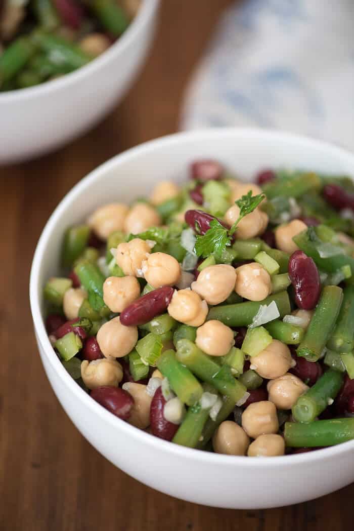 A white bowl filled with Three Bean Salad on a wood surface.
