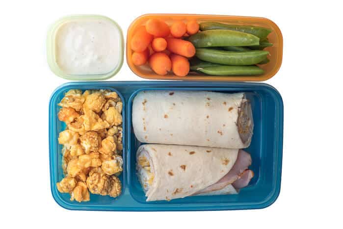 A wrap sliced in half with veggies and dip in a plastic lunch container.