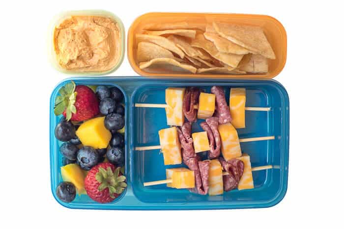 Salami and cheese skewers and fruit in a plastic lunch container.