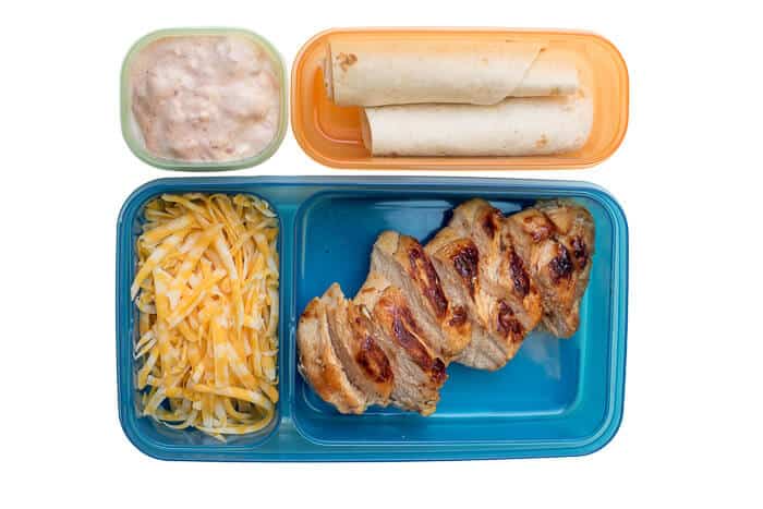 Grilled chicken, shredded cheese, tortillas, and dip in a plastic lunch container.