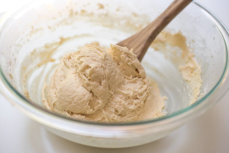 A wooden spoon stirs cake batter in a glass bowl.