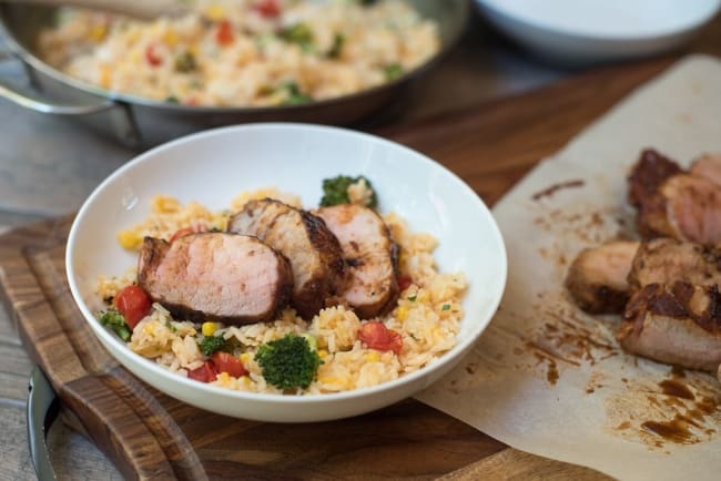 Grilled Pork Tenderloin with Cheesy Vegetable Rice in a white bowl next to sliced pork.