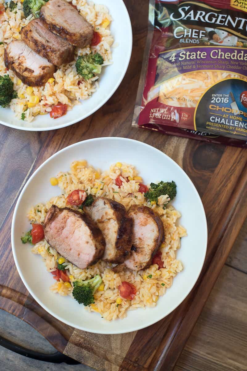 Grilled Pork Tenderloin with Cheesy Vegetable Rice in a white bowl on top of a wood board.