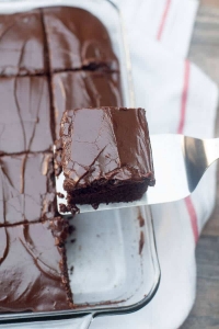 A piece of chocolate cake is lifted with a spatula from a baking dish.