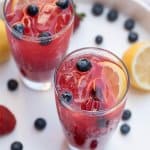 Two glasses filled with berry lemonade, ice and fresh blueberries.