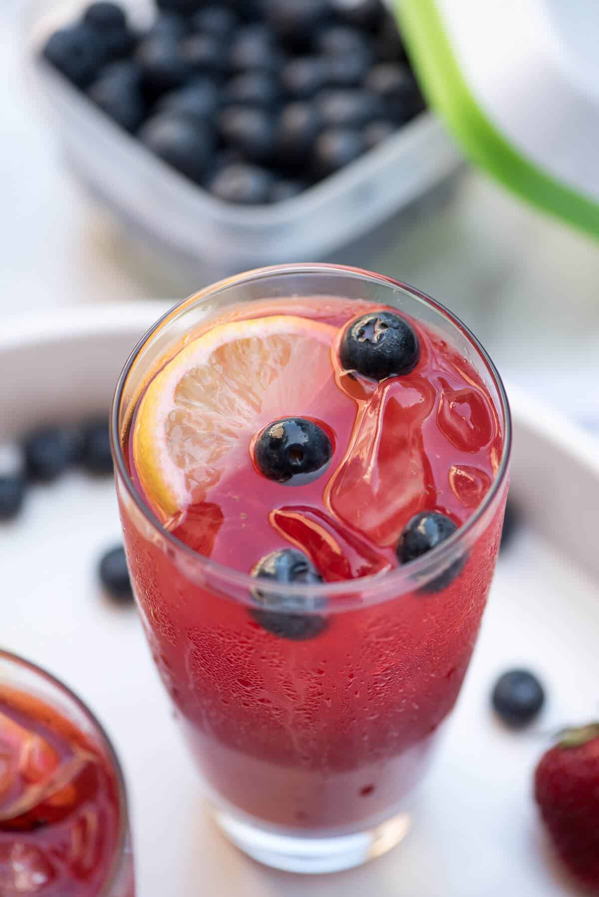 An close up of a glass of Berry Lemonade with lemons slices and blueberries.