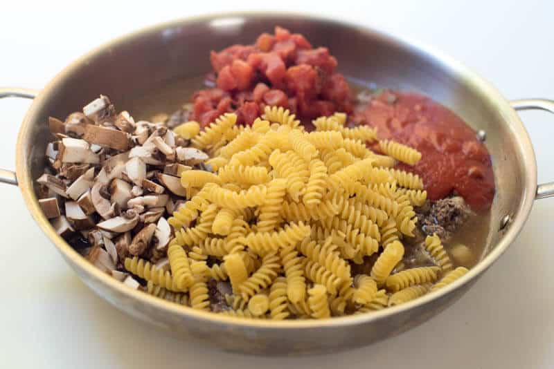 Dry pasta, mushrooms, and other ingredients in a skillet.