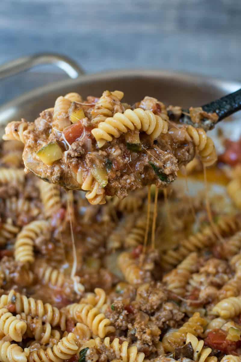 A spoon scoops Cheesy Beef Pasta from a skillet.