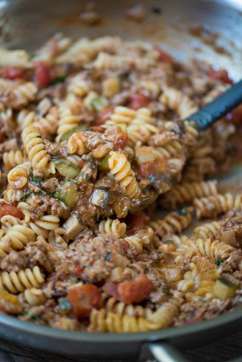 A close up of a spoon scooping up pasta with beef and vegetables.