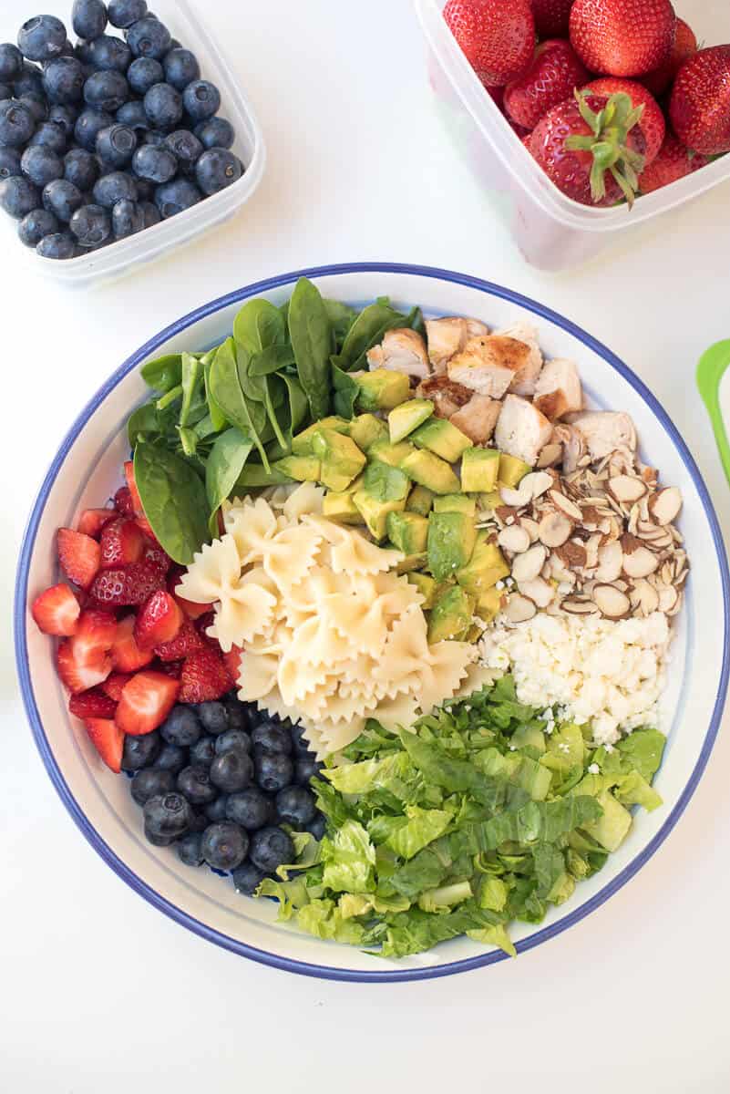 Pasta, berries, spinach, chicken, and other ingredients in a bowl.