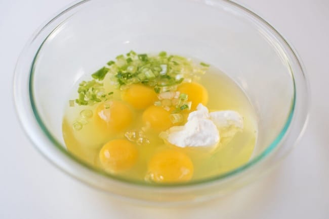Eggs, sour cream and green onion in a glass mixing bowl.