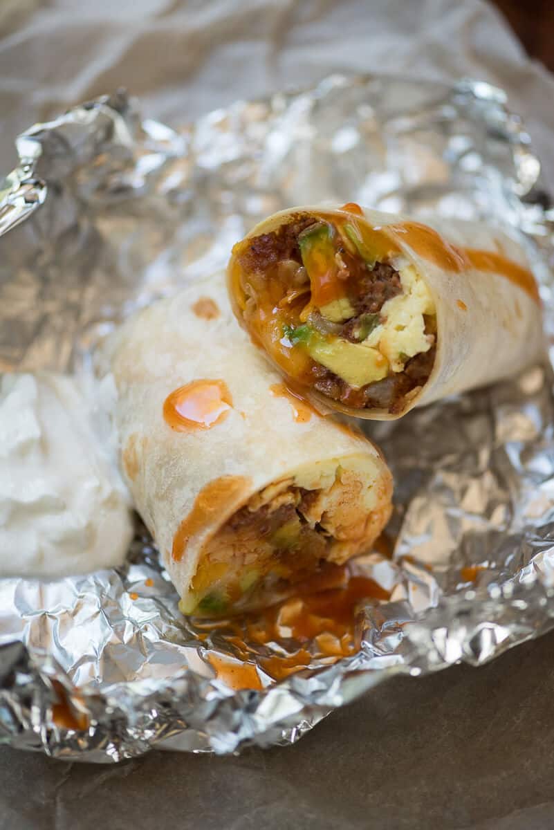 A close up of a Corned Beef Hash Breakfast Burrito sliced in half on top of foil.