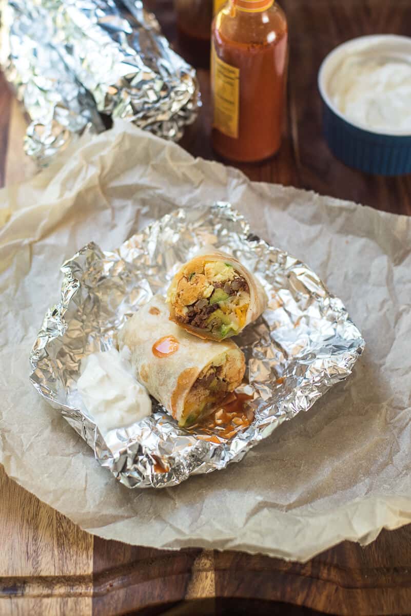 A Corned Beef Hash Breakfast Burrito sliced in half on top of foil with sour cream.