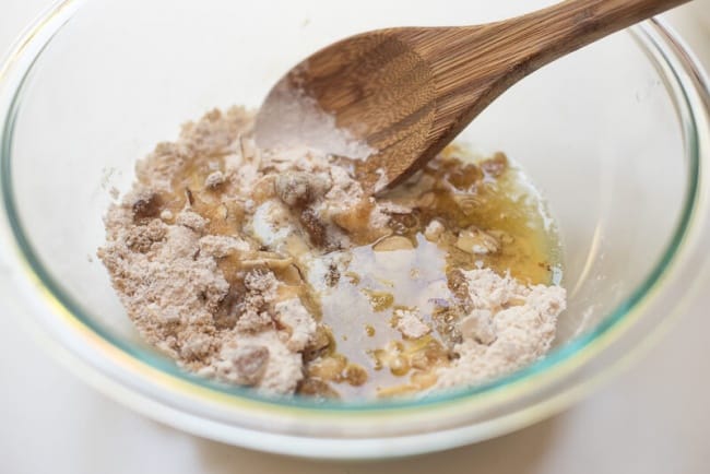 A spoon stirs melted butter into a dry mixture in a glass bowl.