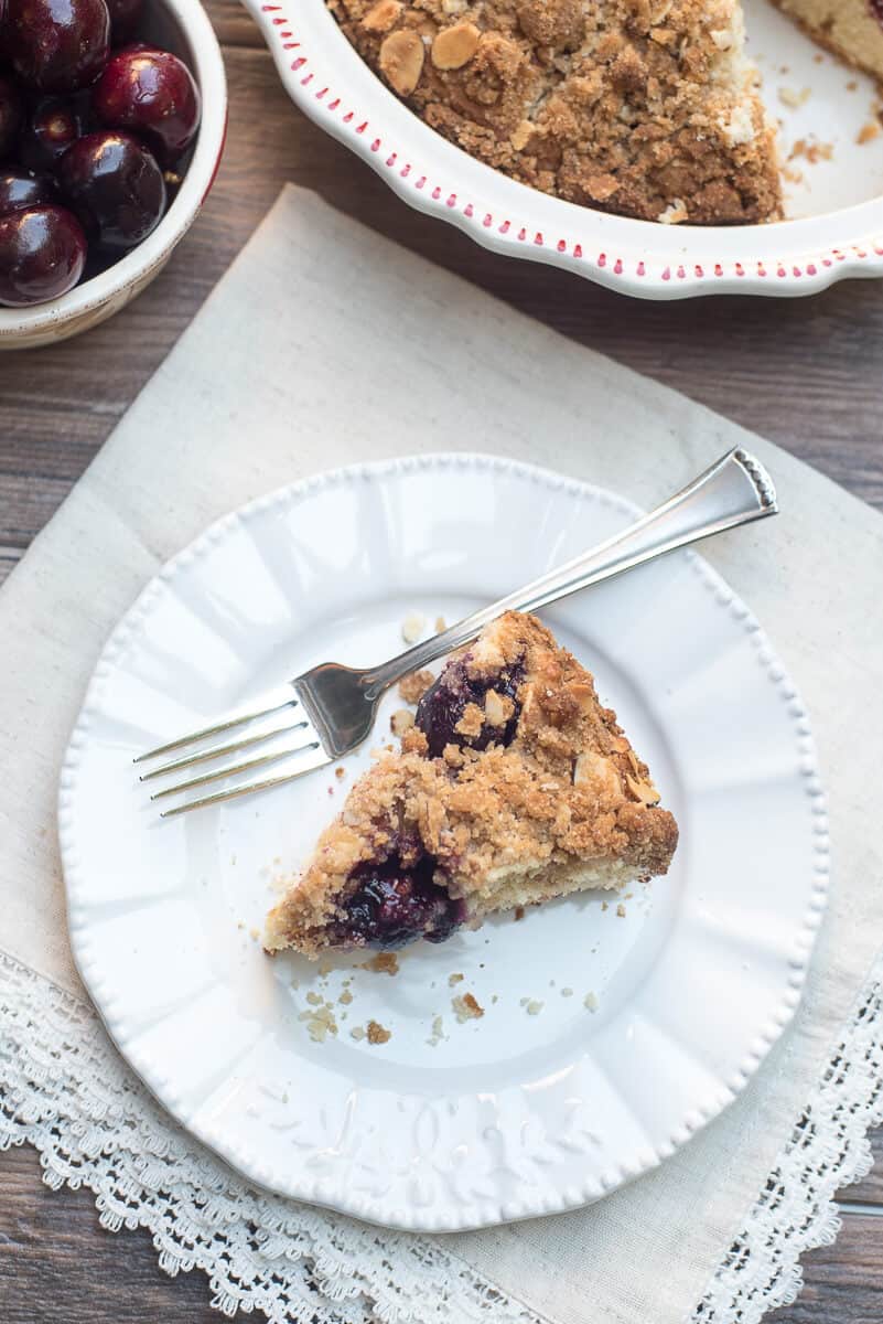 A slice of Fresh Cherry Crumb Cake on a white plate with a fork.