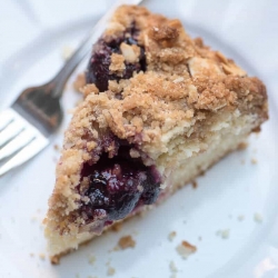 A slice of cherry crumb cake on a white plate with a fork.