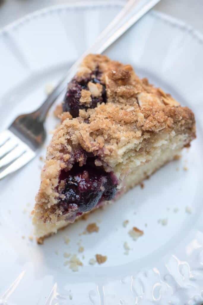 A slice of cherry crumb cake on a white plate with a fork.