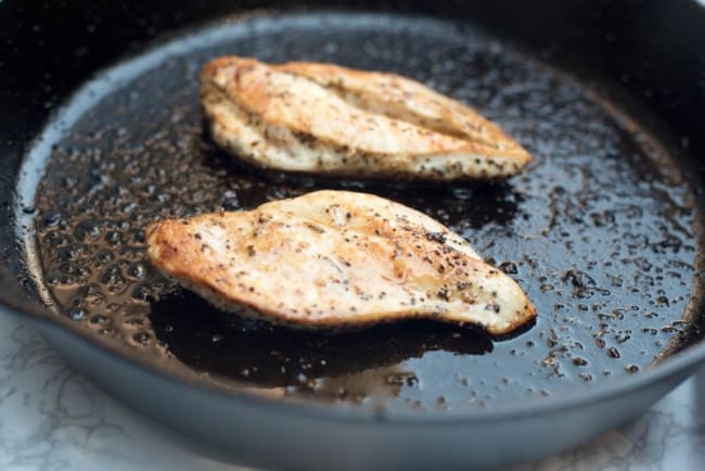 Seasoned chicken cooking in a cast iron skillet.