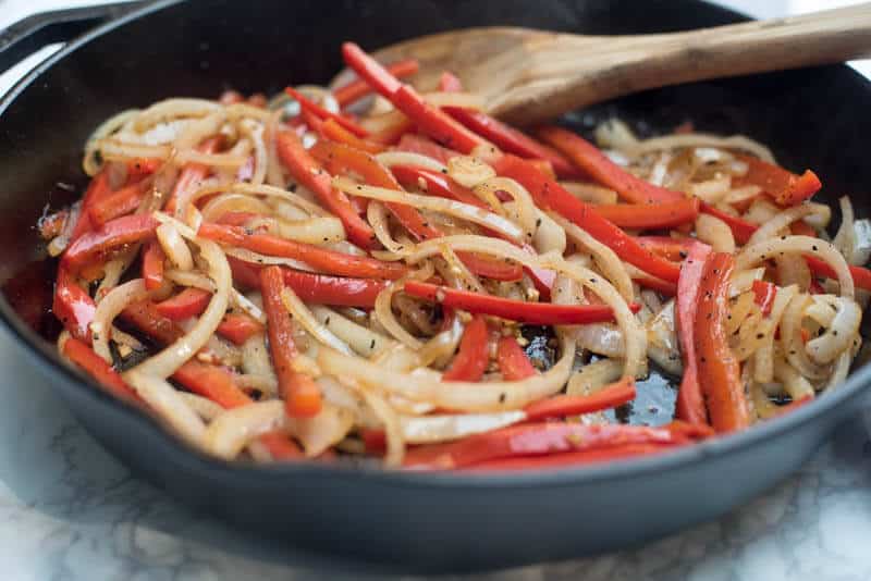 Bell peppers and onions cooking in a cast iron skillet.