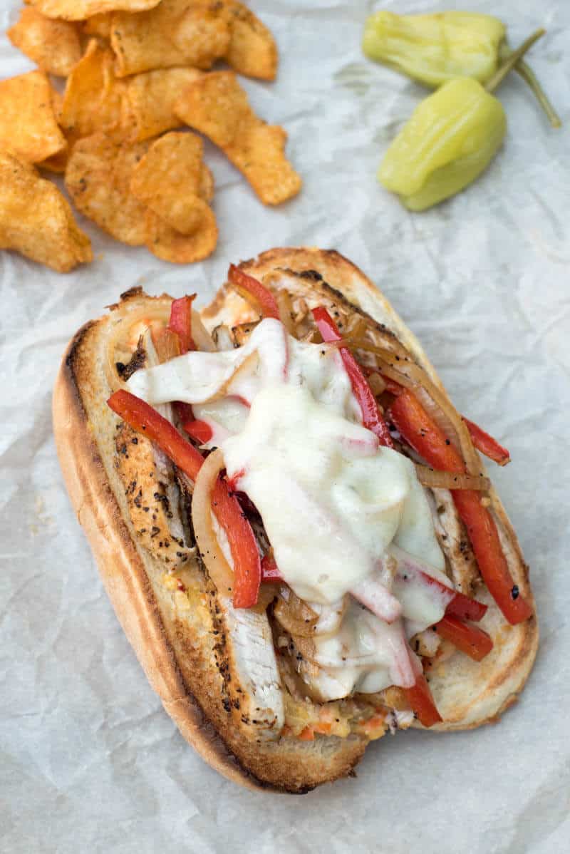 An assembled Italian Chicken Sub on parchment paper with potato chips and peppers in the background.