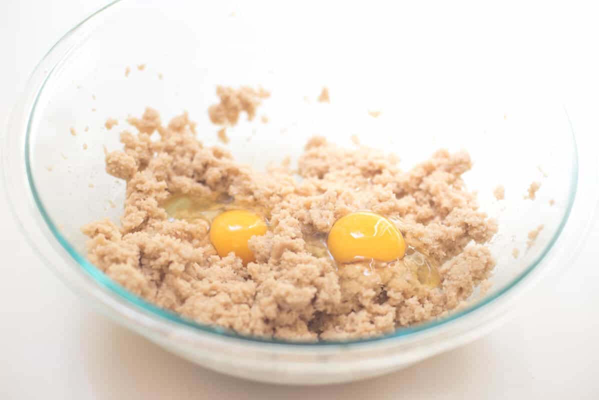 Eggs are added to the wet ingredients in a glass mixing bowl.