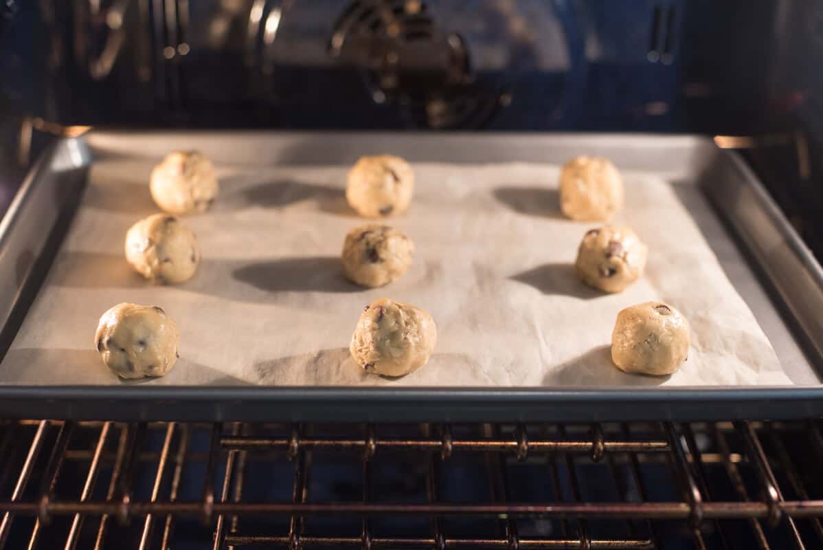 Balls of cookie dough on a parchment paper lined baking sheet in the oven.