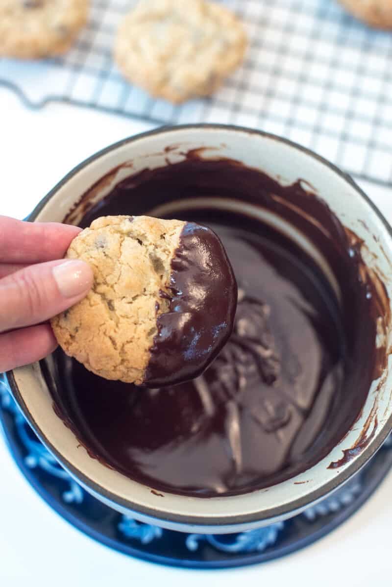 A hand holds a cookie that has been dipped in the melted chocolate.