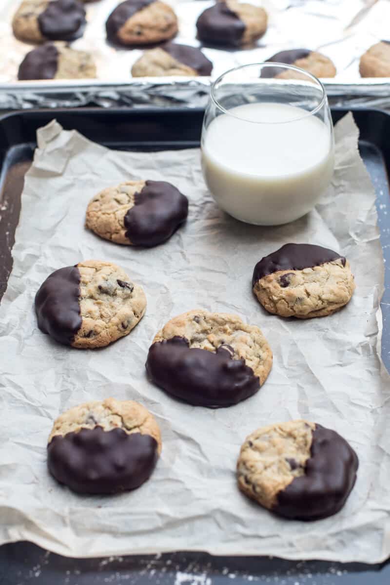 Chewy Chocolate Dipped Oatmeal Cookies on a parchment paper lined baking sheet with a glass of milk.