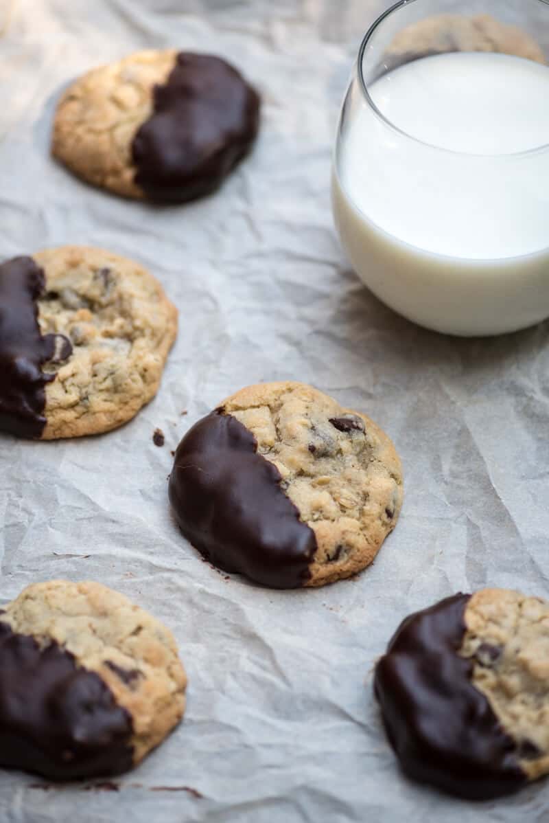 Chewy Chocolate Dipped Oatmeal Cookies on a piece of parchment paper with a glass of milk.