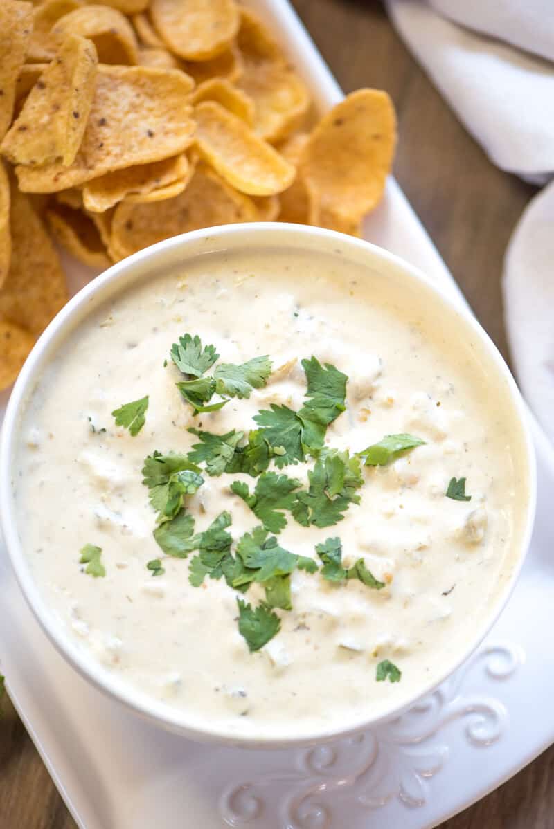 A closeup of cheesy dip topped with cilantro in a white bowl next to corn chips.