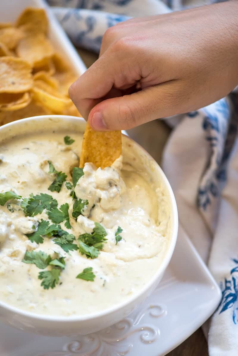 A hand dipping a corn chip into queso dip.