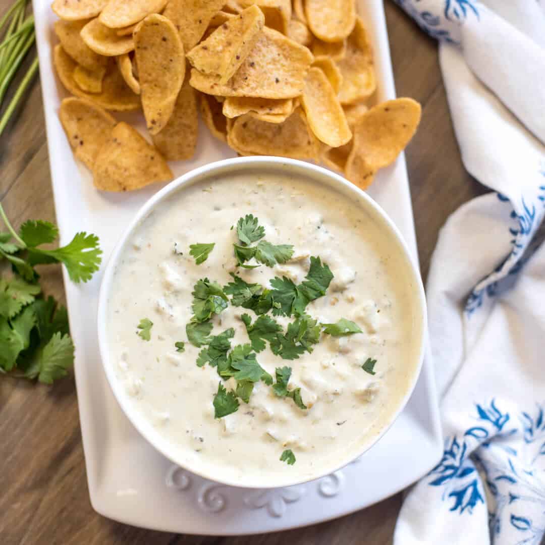 Easy Queso Verdeo in white bowl topped with cilantro with Frito's corn chips next to it.