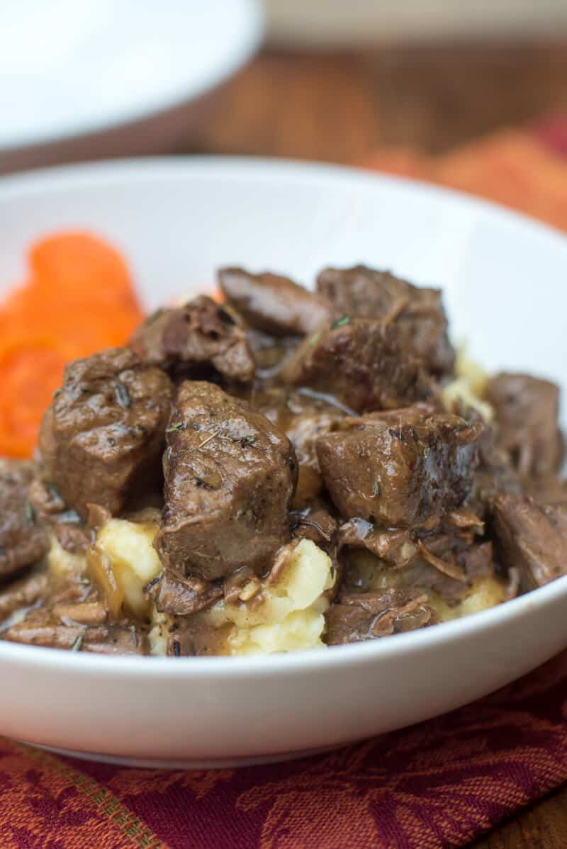 The beef tips with gravy spooned over a mound of mashed potatoes in a white serving bow.