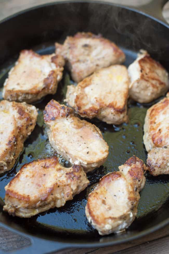 The pork medallions cooking in a cast iron skillet.