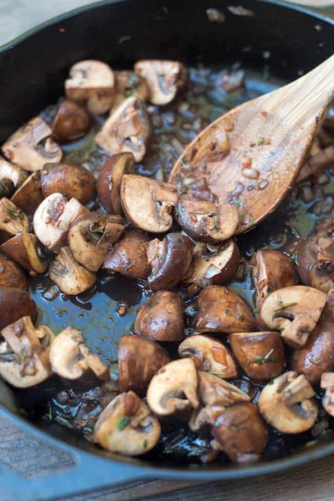 A spoon stirs the mushroom mixture in the skille.