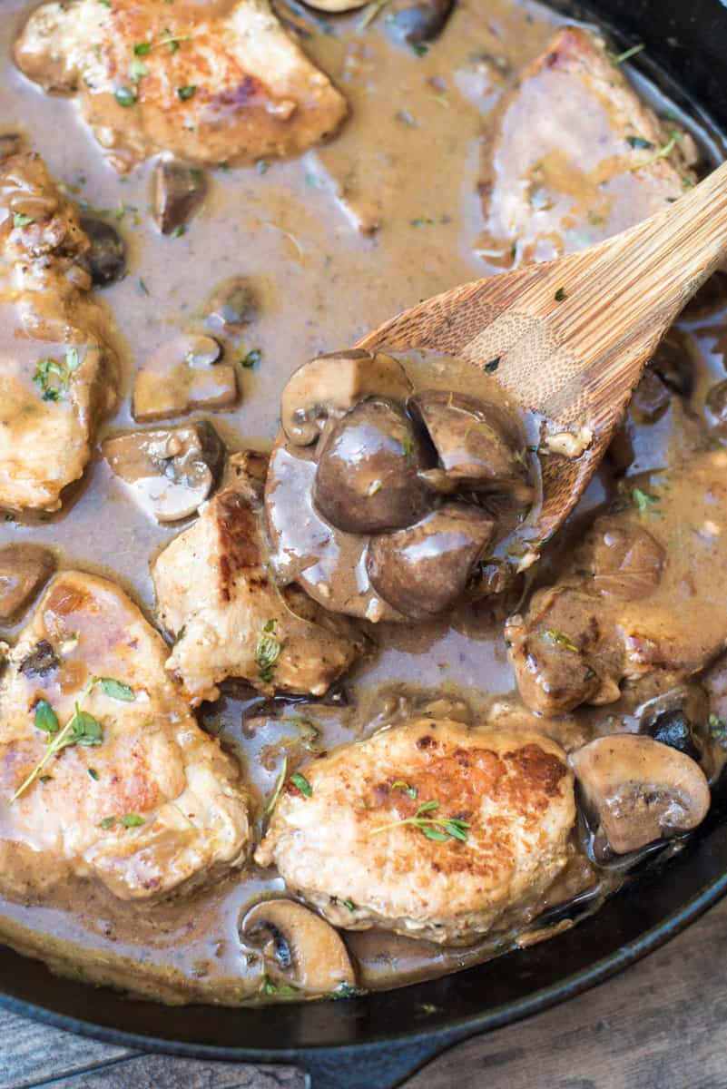 A wooden spoon scoops up some of the mushroom sauce from the skillet.