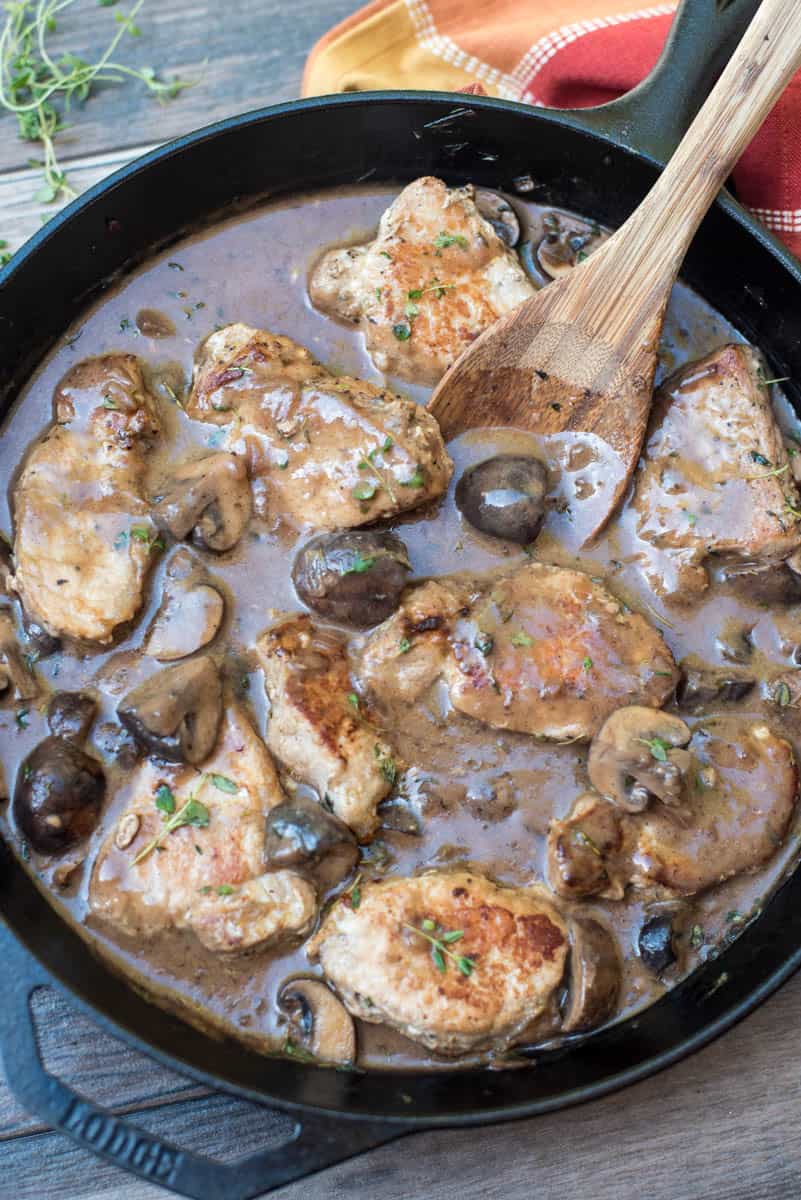 Steakhouse Mushroom Pork Loin Medallions in a cast iron skillet with a wooden spoon.