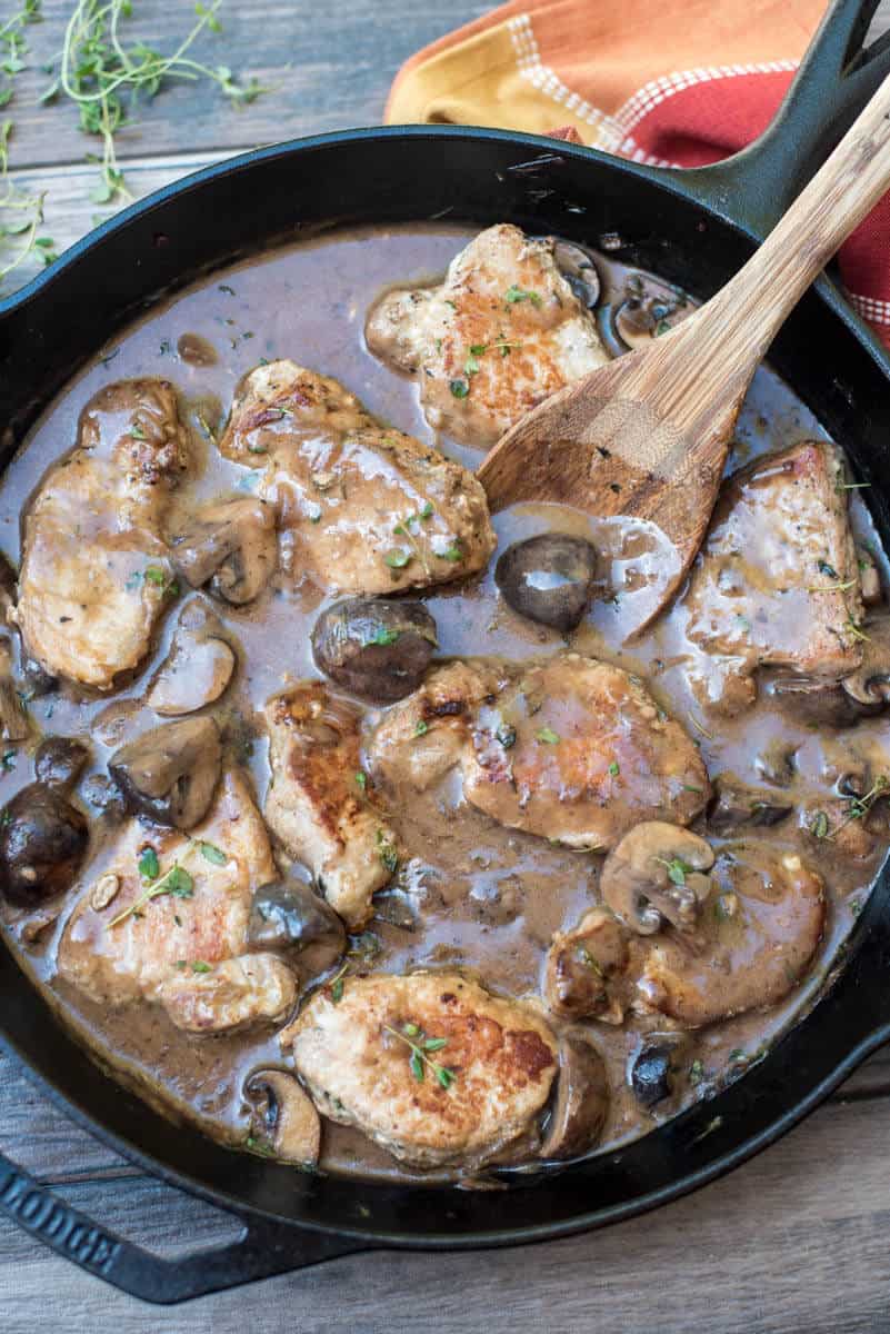 The skillet full of pork medallions and the mushroom sauce with a wooden spoon.