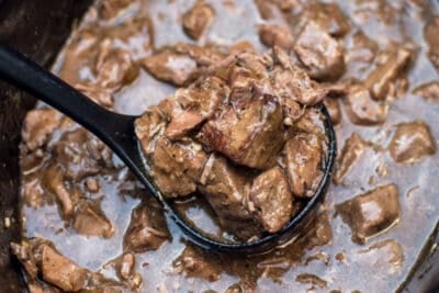 A ladle scooping beef tips with gravy from a slow cooker.