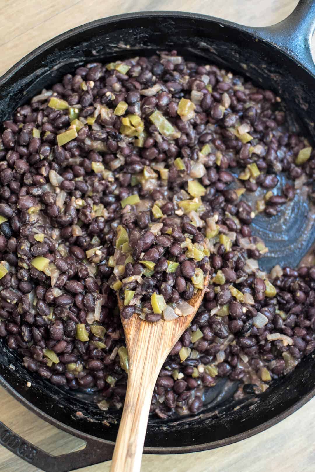 Easy Cuban-Style Black Beans in a skillet with a wooden spoon shot from over the top.