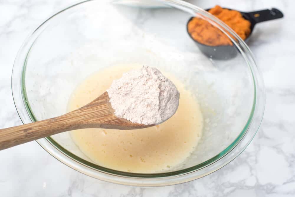 Flour is added to wet ingredients in a mixing bowl.