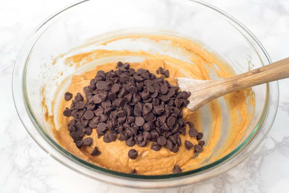 Chocolate chips are stirred in pumpkin muffin batter in a mixing bowl.