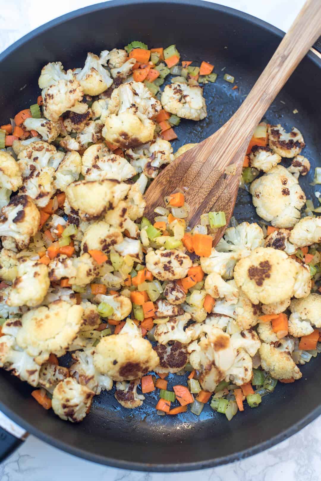 Roasted cauliflower, onion, carrots, and celery cook in a skillet.