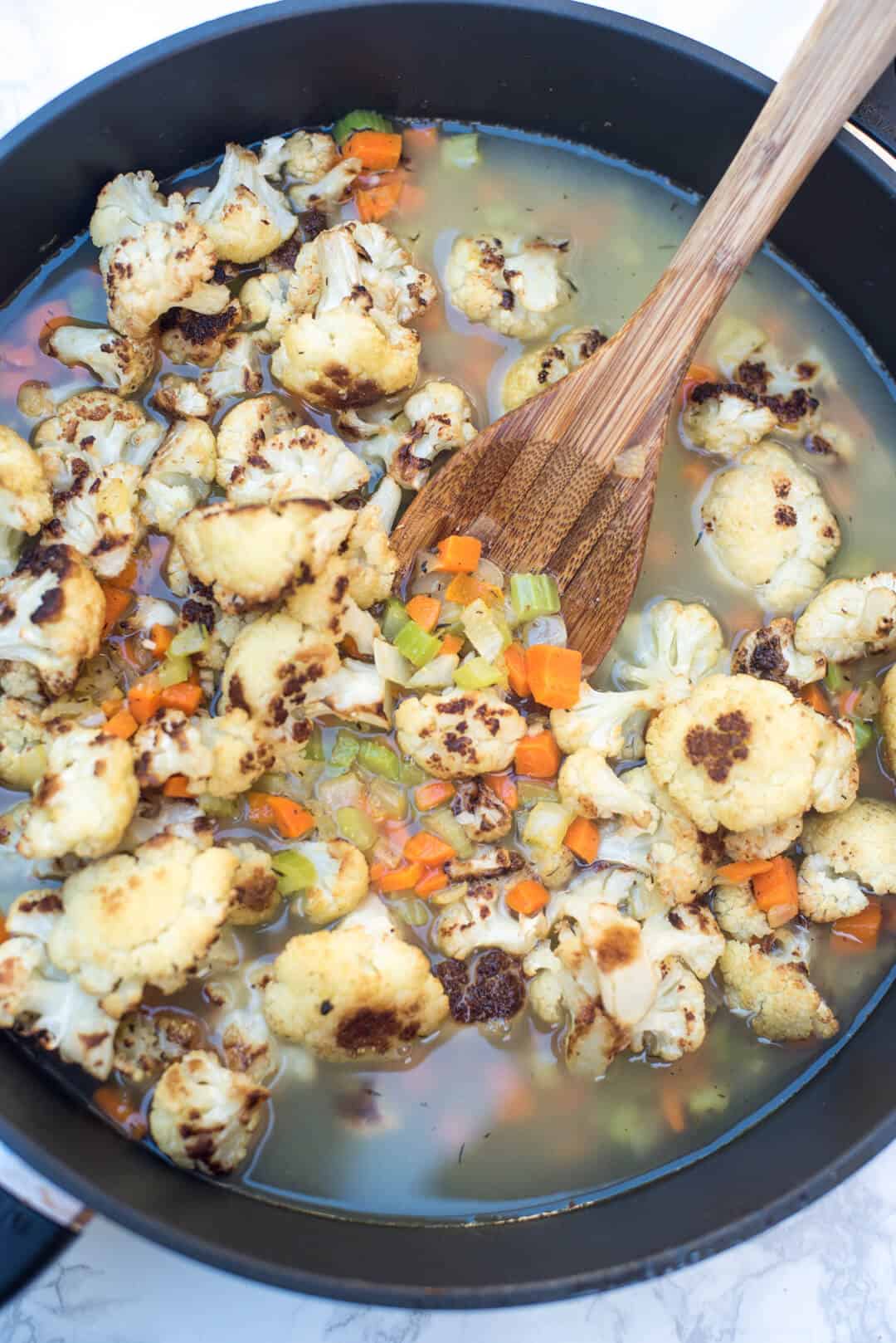 Broth in a skillet with cauliflower and other vegetables.