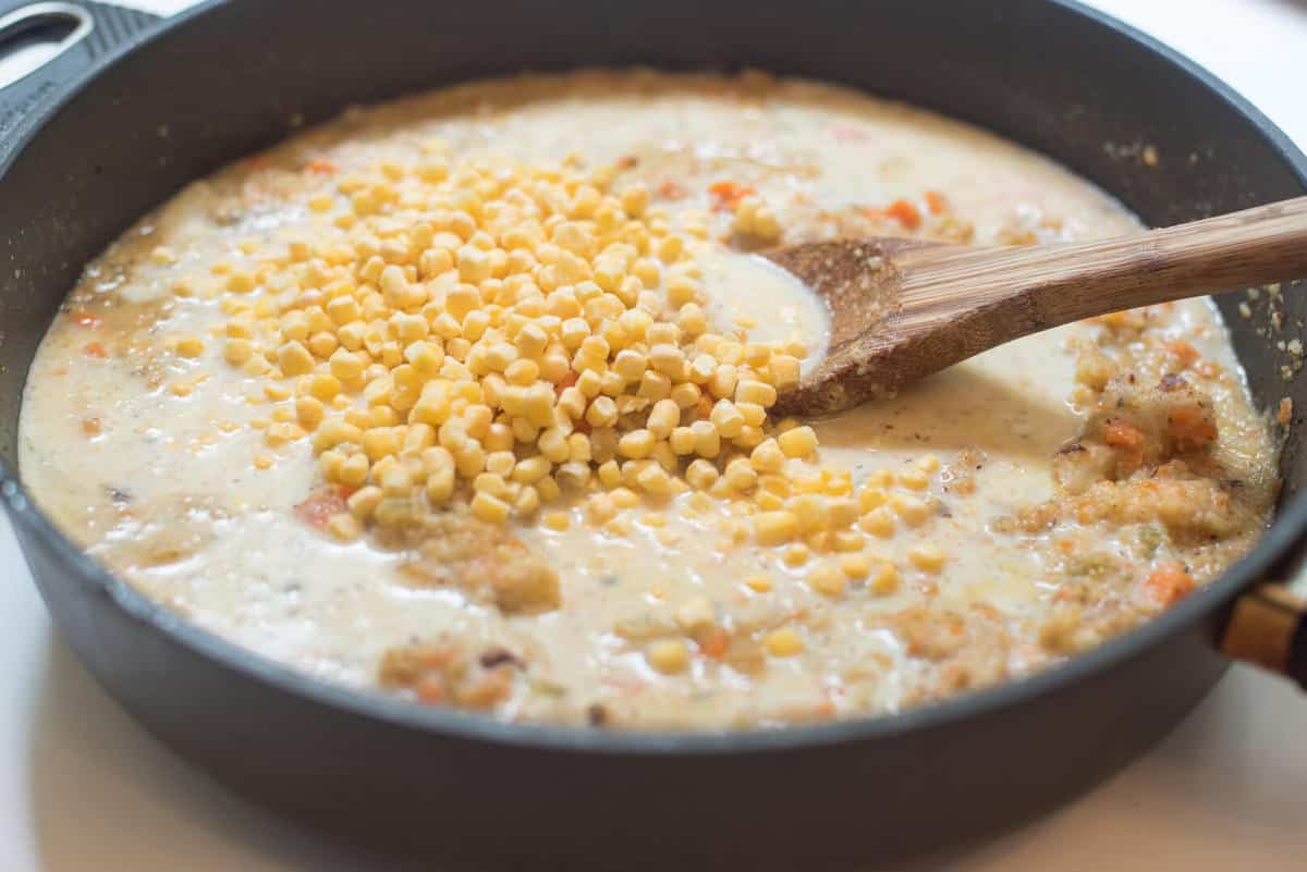 Corn is added to a soup mixture in a skillet.