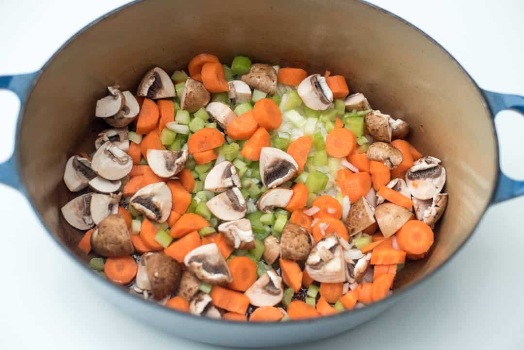Carrots, celery, onion, and mushrooms cooking in a Dutch oven.
