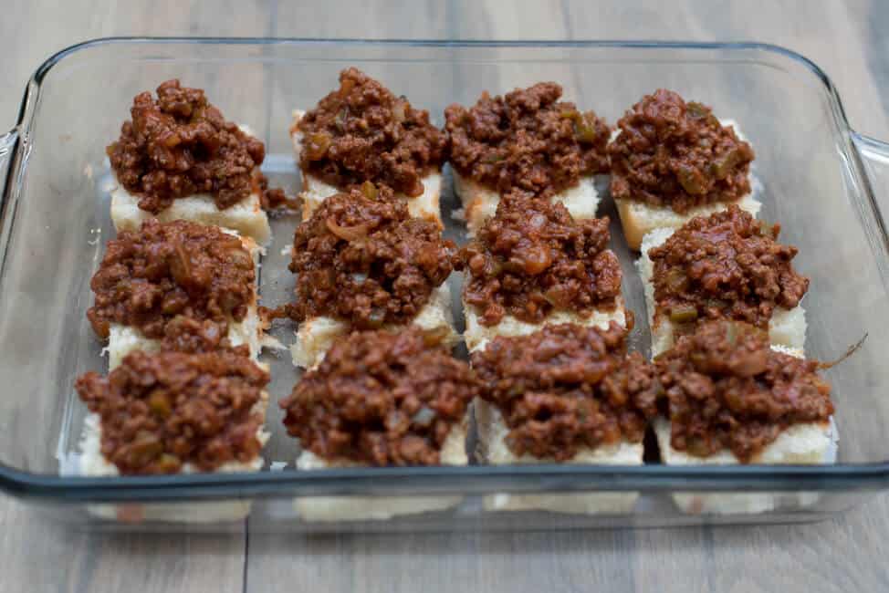 The bottom half of the buns in a casserole dish topped with sloppy joe mixture.