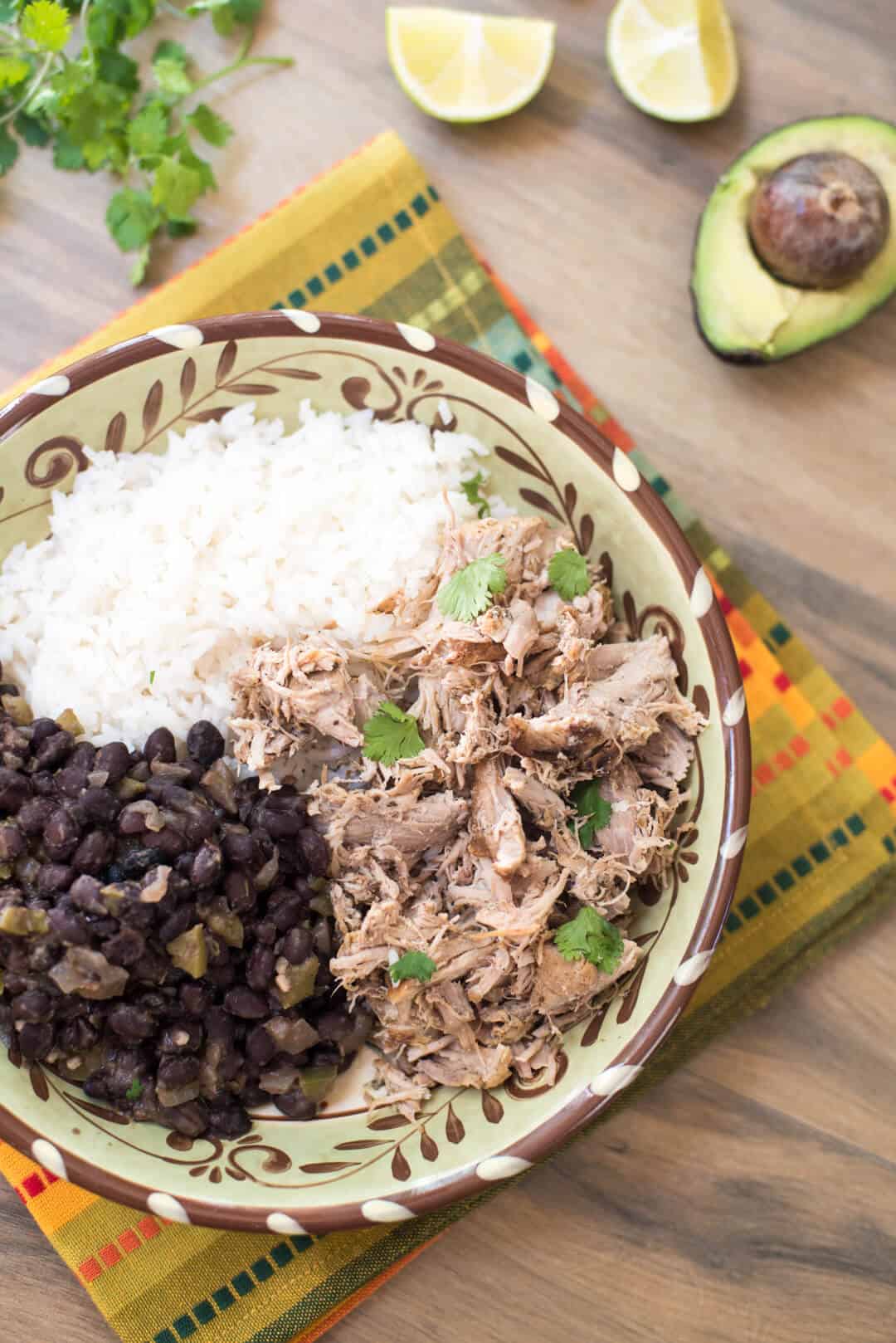 Slow Cooker Cuban Pork with Black Beans and white rice in a patterned bowl on an orange and green patterned cloth.