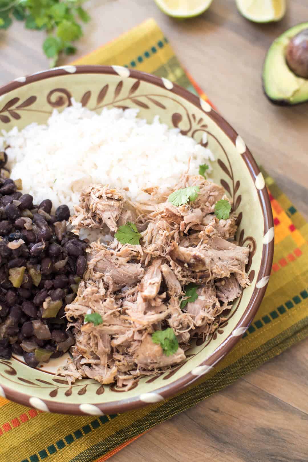 Slow Cooker Cuban Pork with Black Beans with white rice in a bowl on a patterned cloth.